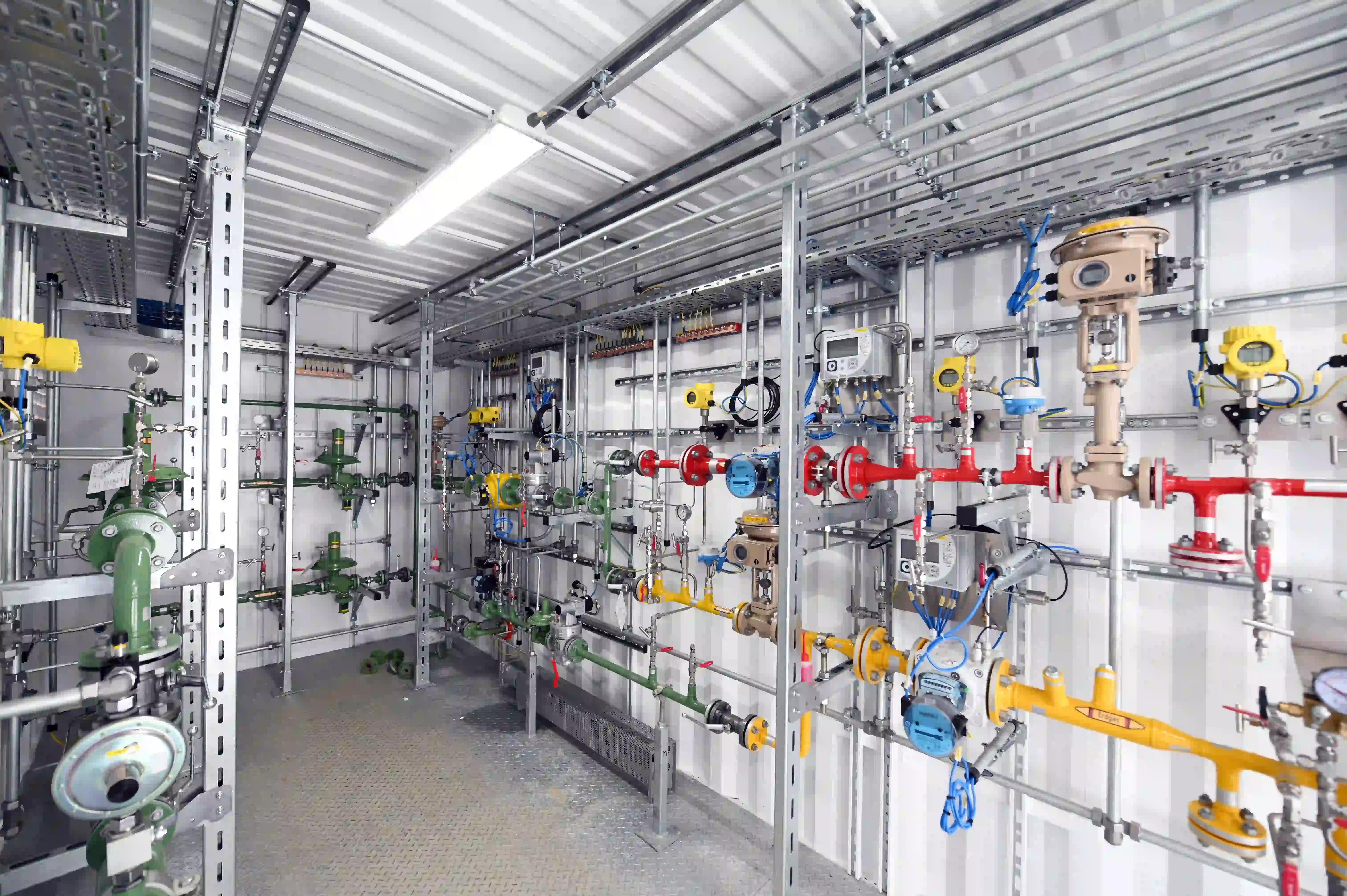 Technischer Raum mit zahlreichen farbigen Rohrleitungen, Ventilen und Messgeräten zur Gas- oder Flüssigkeitssteuerung.
