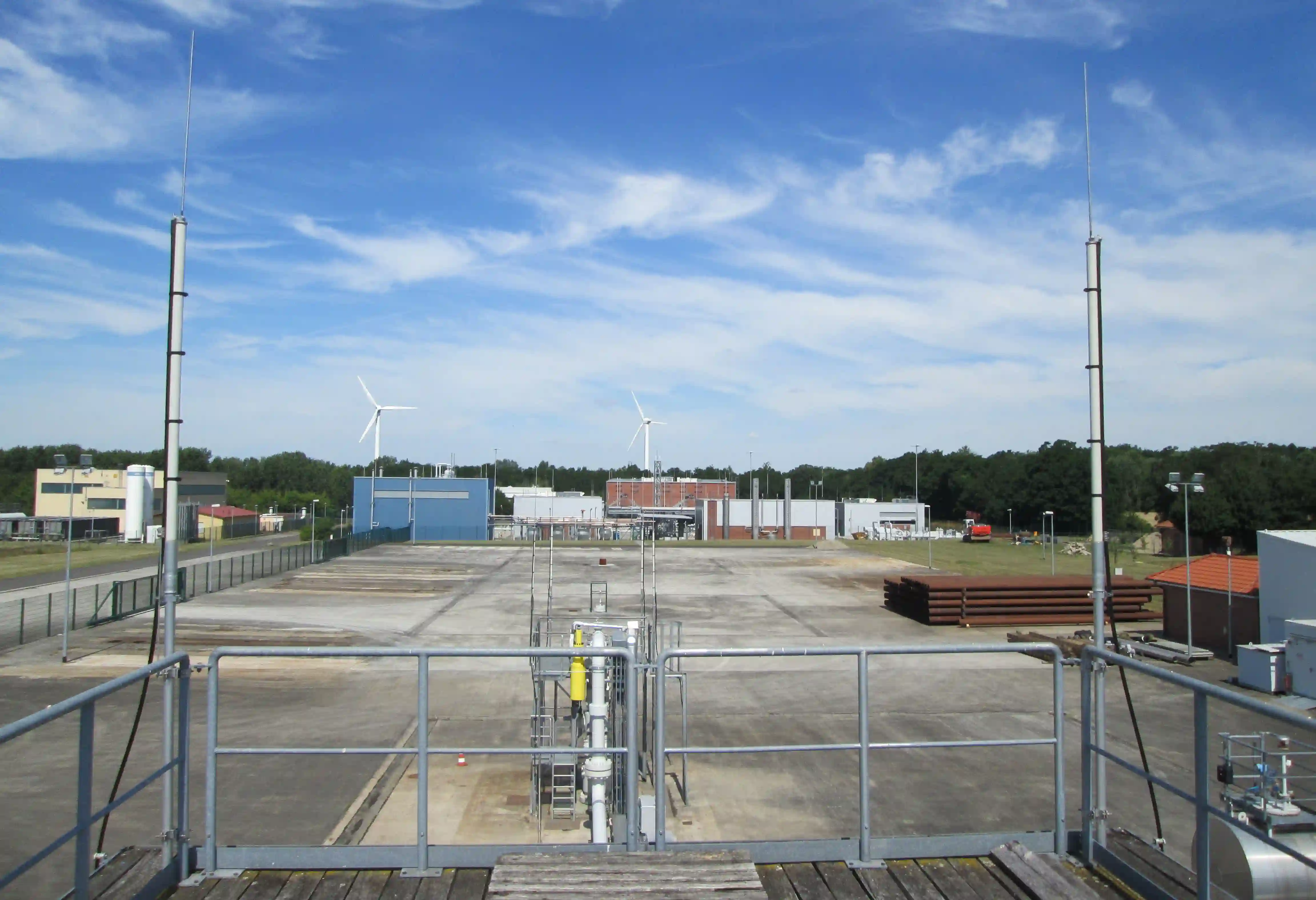 Erdgasspeicher-Anlagenplatz mit Kavernen, Rohrleitungen, Windkraftanlagen im Hintergrund und Industriegebäuden unter...