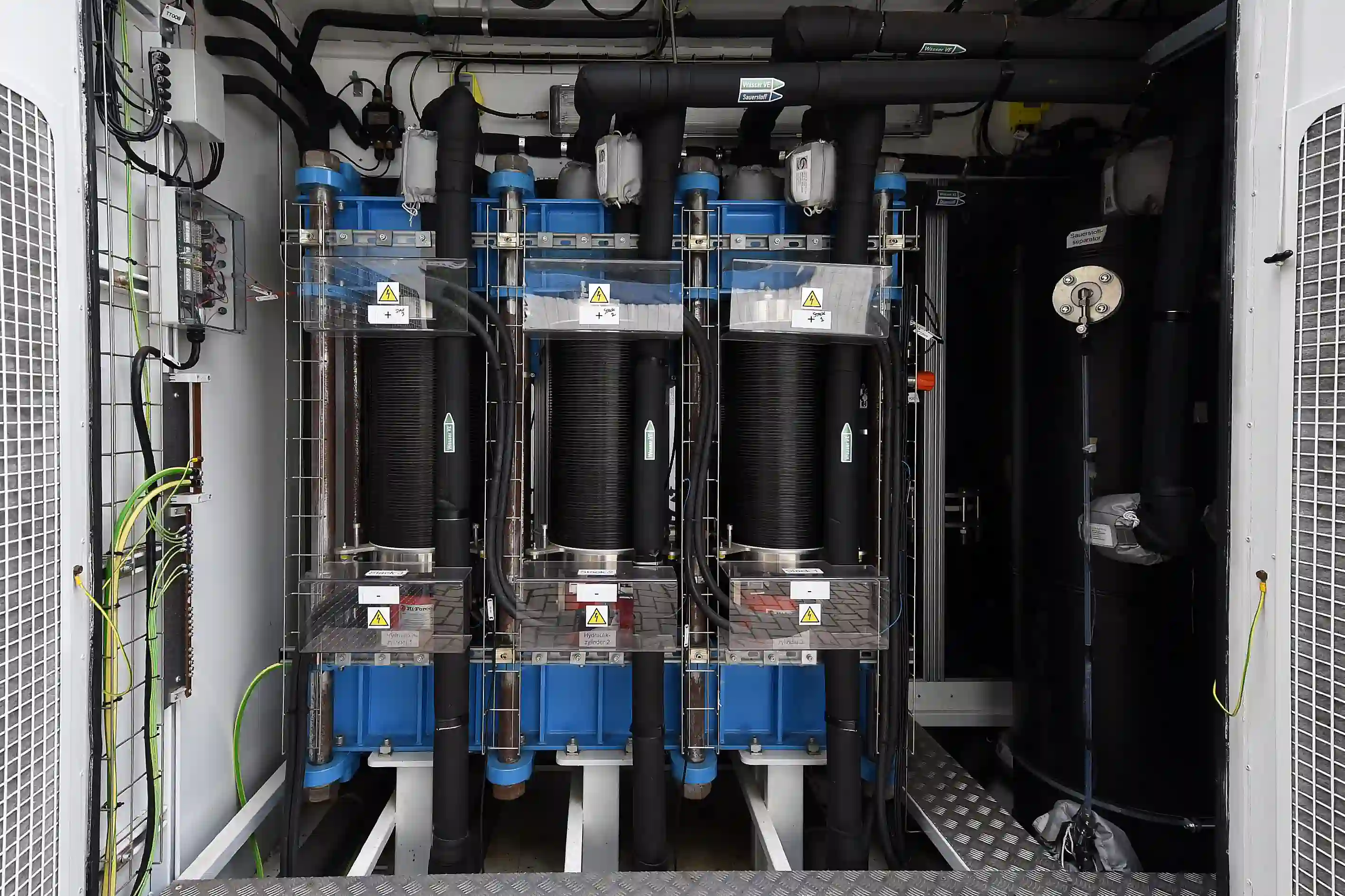 Innenansicht einer Power-to-Gas-Anlage mit drei großen schwarzen Behältern, blauen Komponenten und Rohrleitungen
