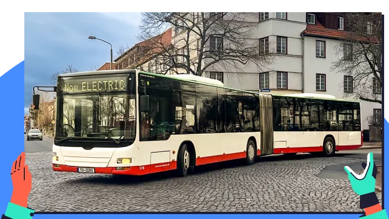Ein elektrischer Gelenkbus fährt auf einer gepflasterten Straße an Wohnhäusern vorbei.