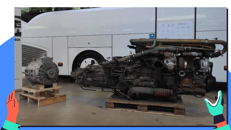 Ein ausgebauter Verbrennungsmotor mit Getriebe steht auf Paletten vor einem Reisebus.