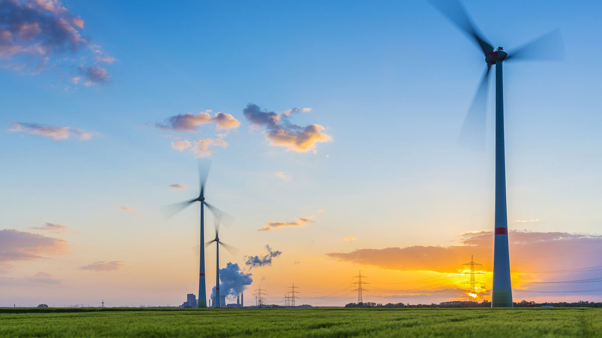 Windräder vor Kohlekraftwerk und blauem Himmel