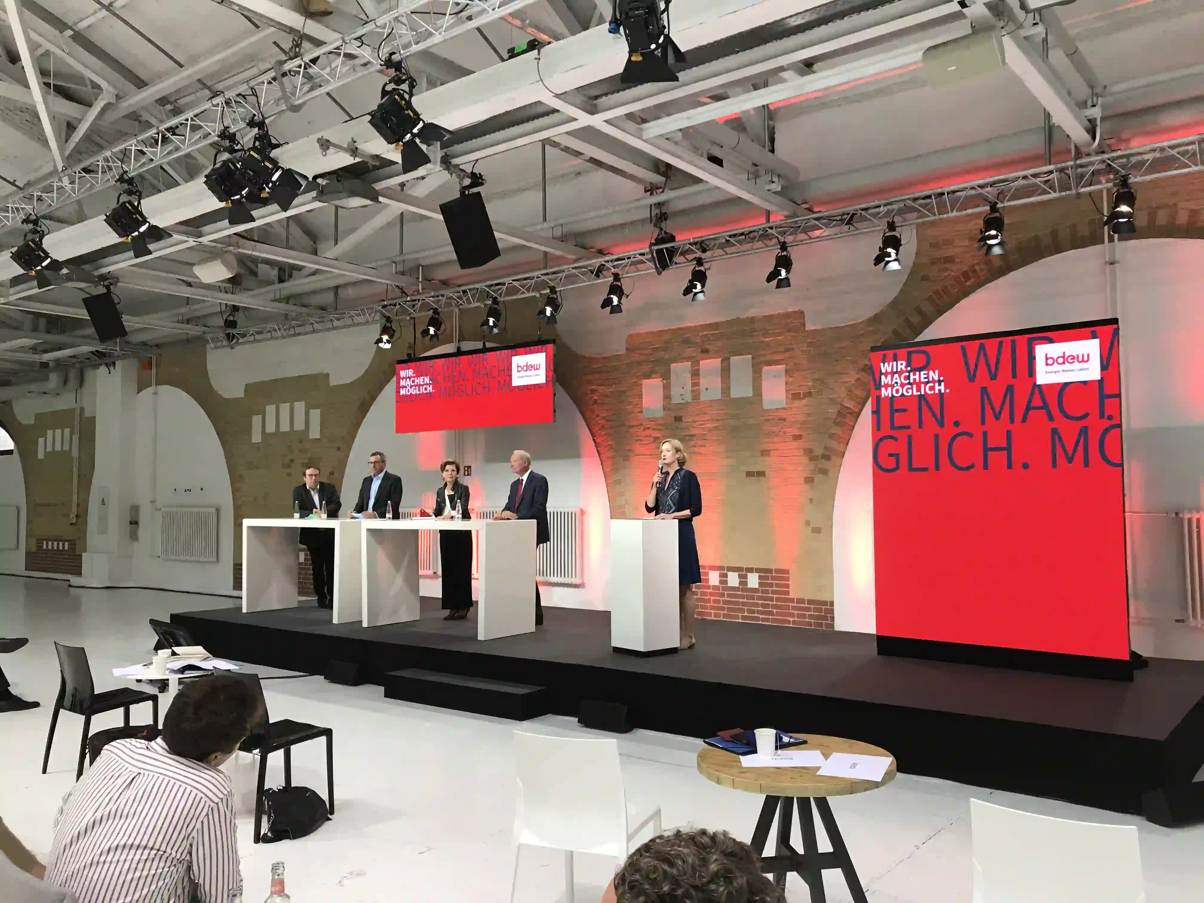 Podiumsdiskussion mit fünf Personen auf einer Bühne, rote Bannerwand mit BDEW-Logo, Publikum im Vordergrund,...